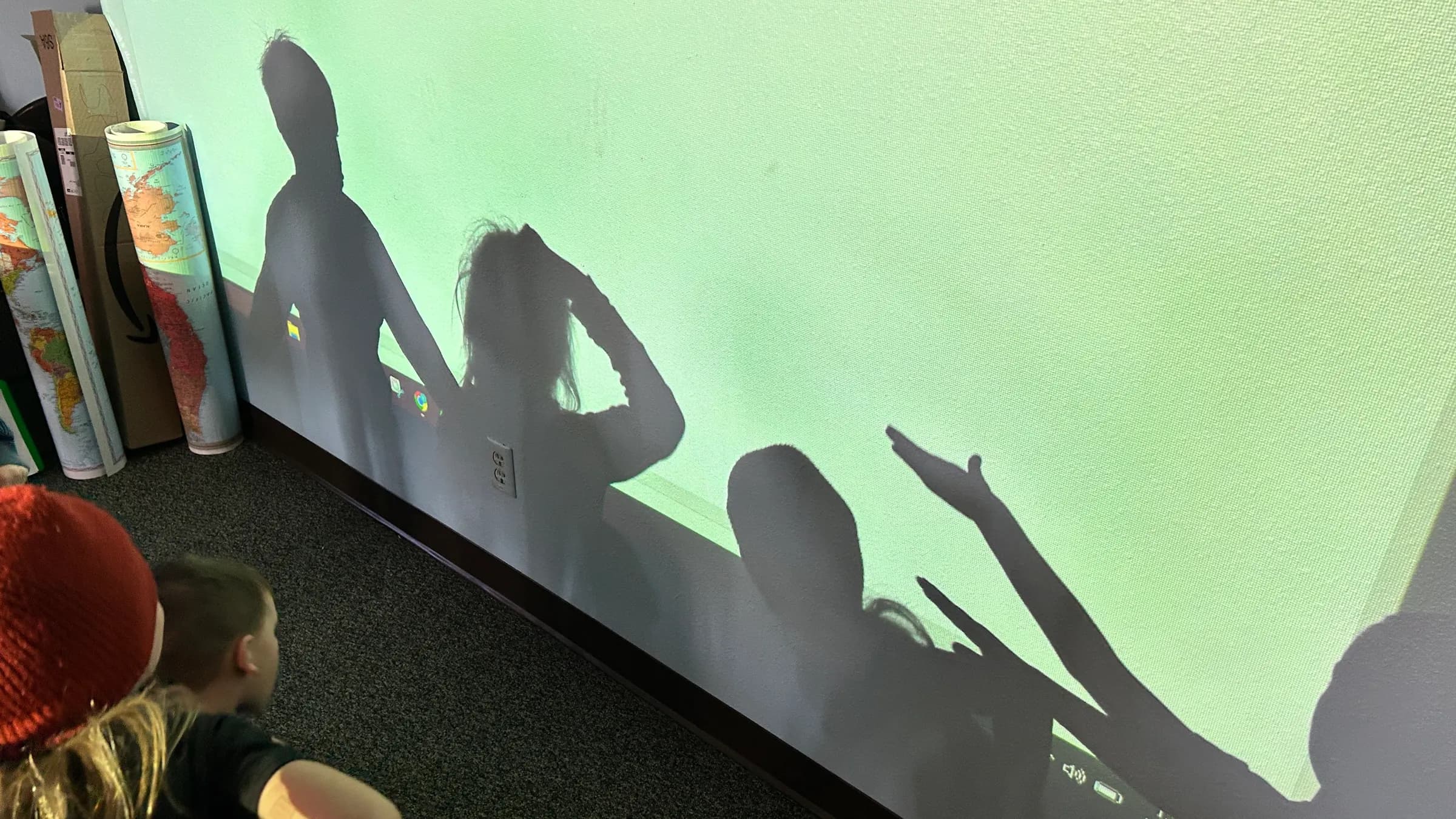 Children make shadow shapes on a green-lit projector screen during a SPRUCE class.