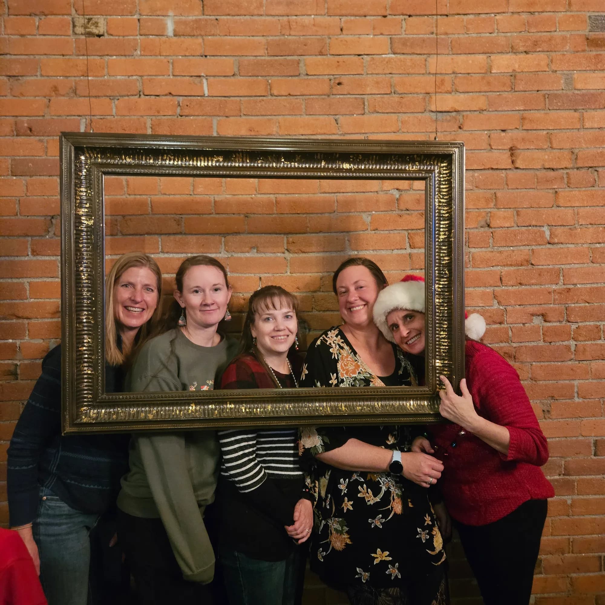 Five SPRUCE staff members smiling inside a gilt picture frame against a brick wall.