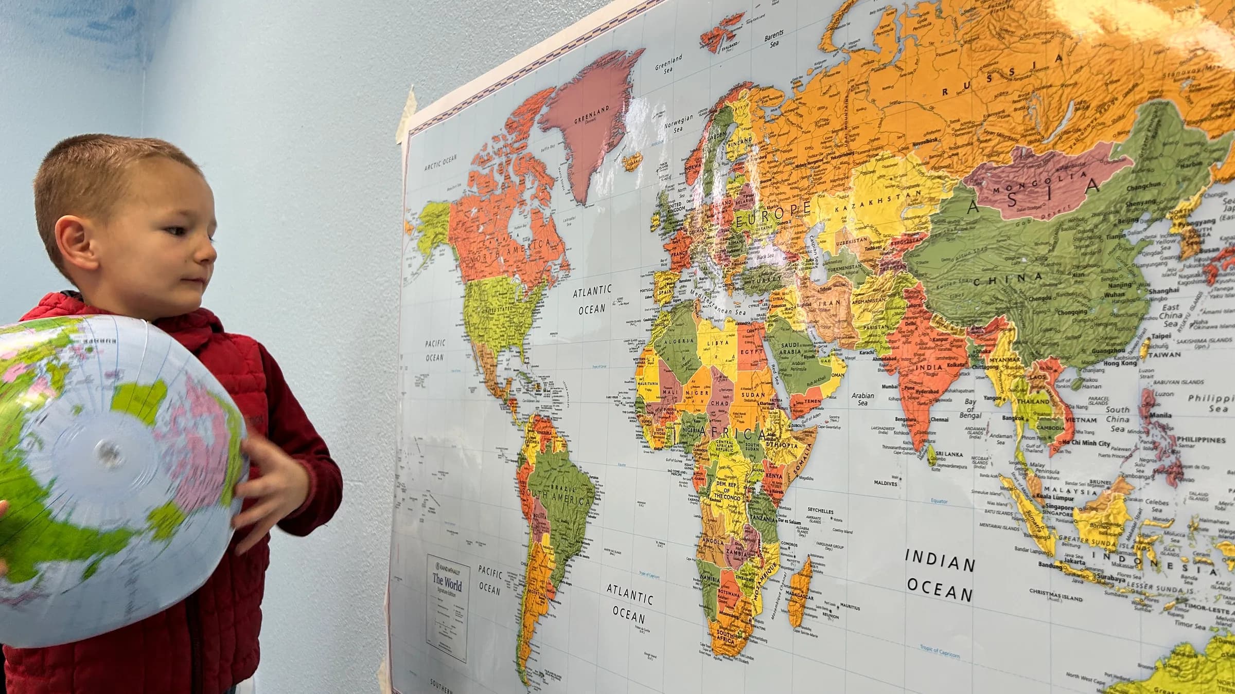 A young SPRUCE student holds an inflatable globe beside a world map.